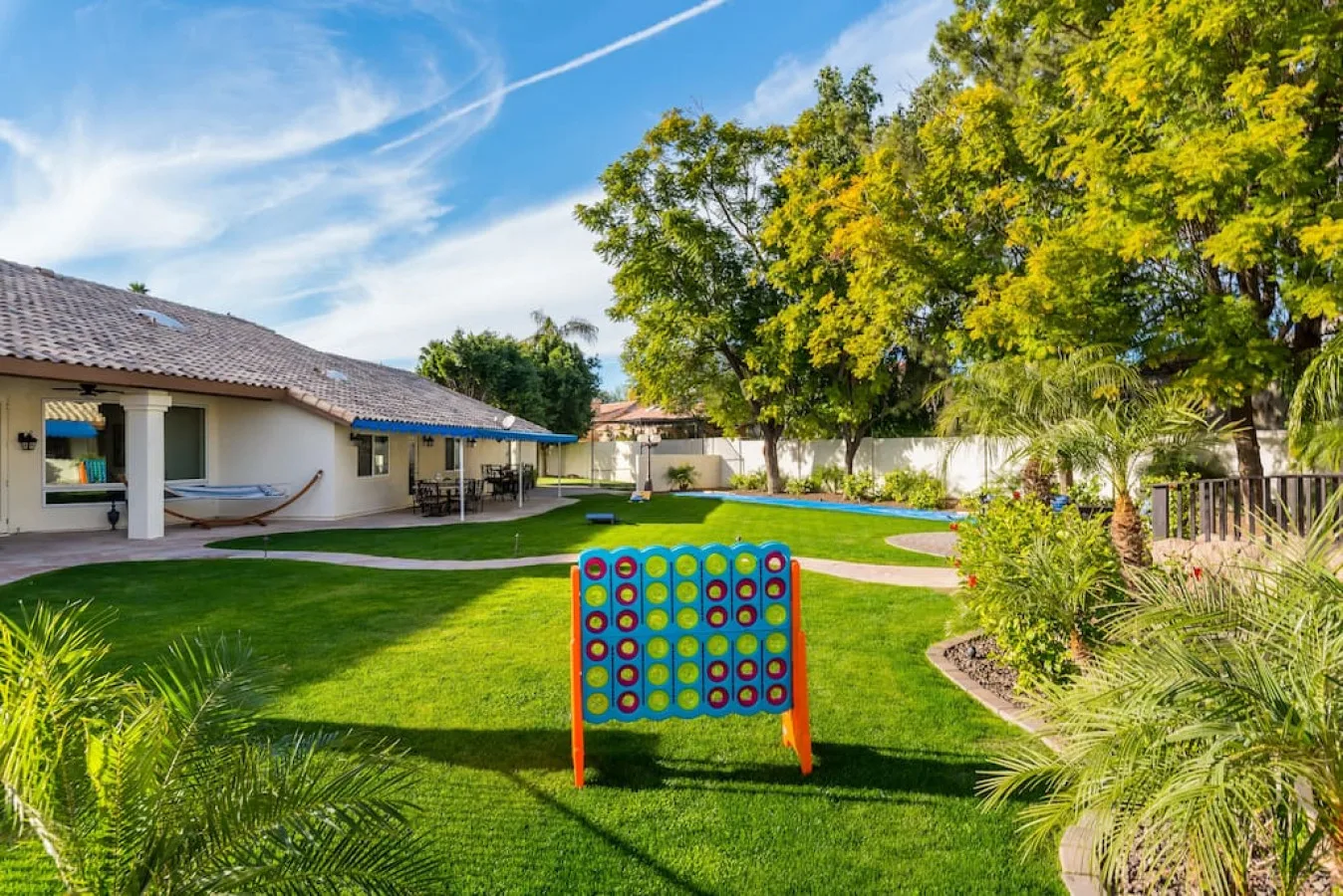 Un patio ajardinado con césped, árboles y un tablero de juego colorido.