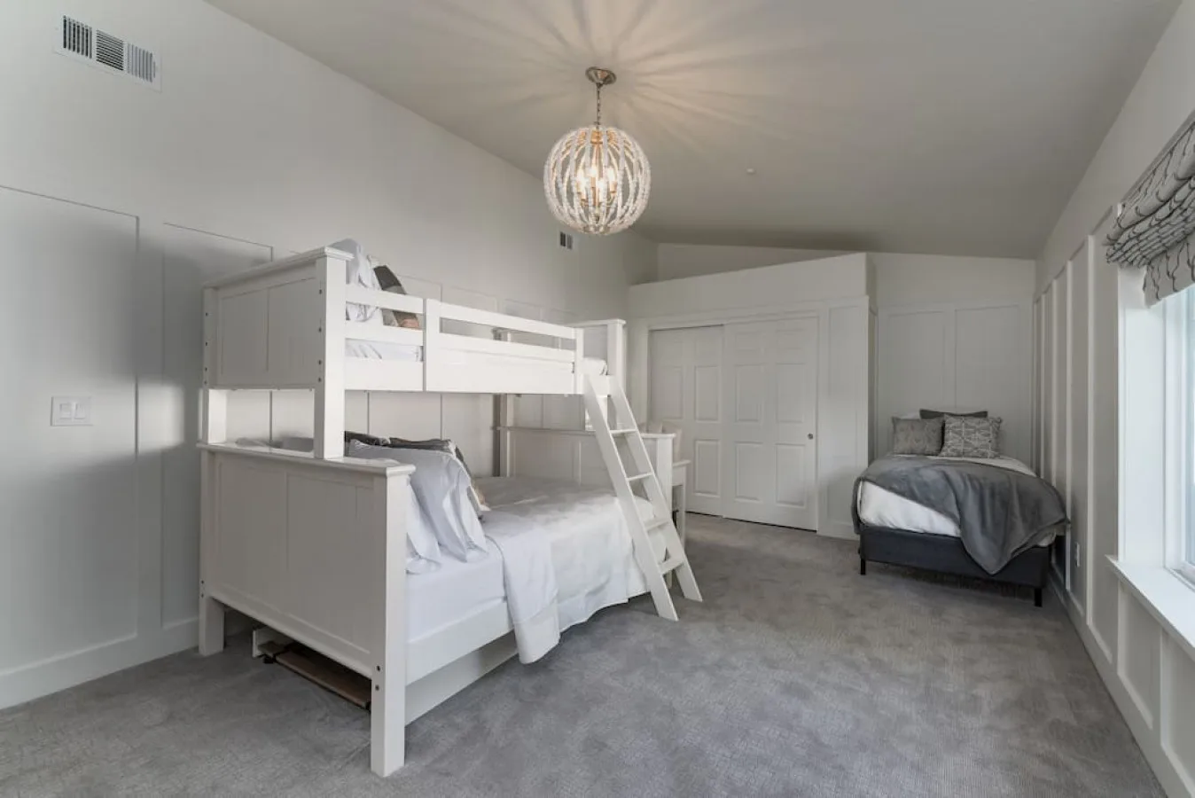 Un dormitorio con una litera blanca, otra cama y alfombra gris.