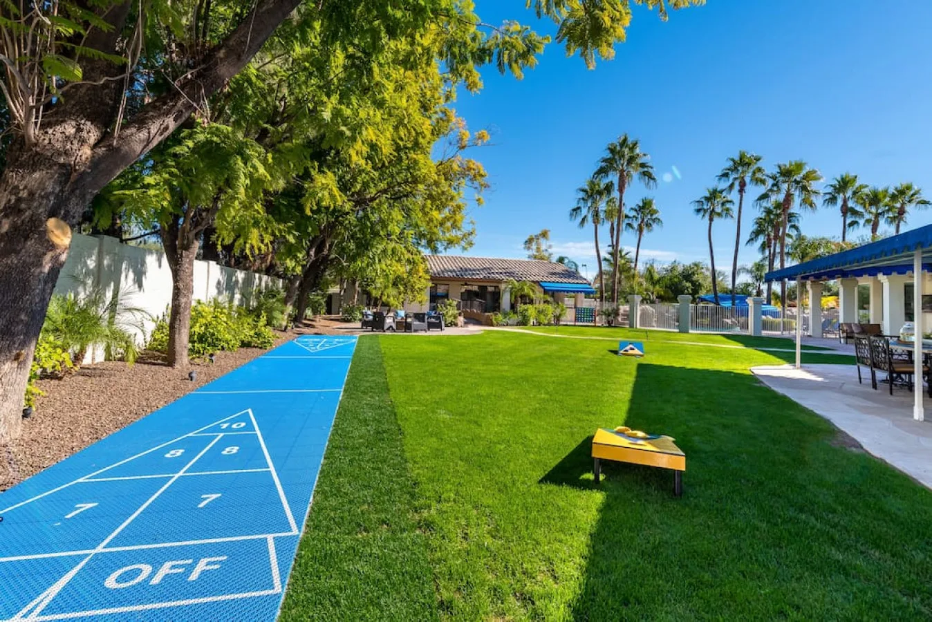Una zona recreativa al aire libre con cancha azul, césped verde y asientos a la sombra.