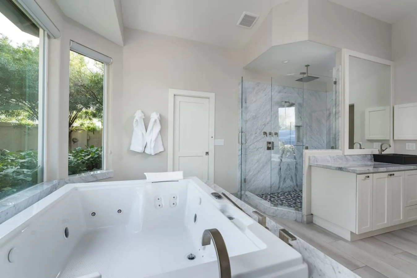 Un baño luminoso con una bañera de hidromasaje grande y una ducha de vidrio.