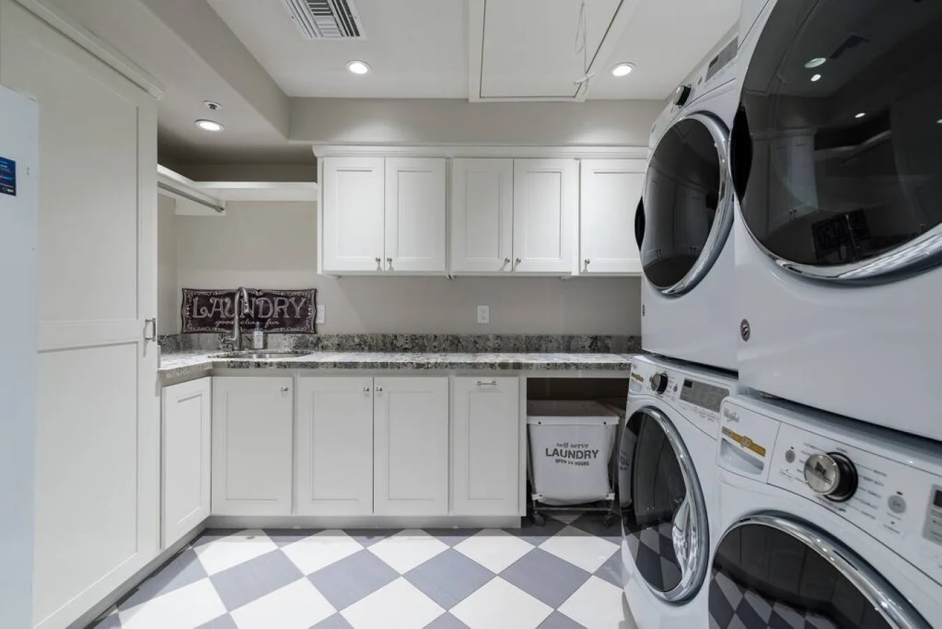 Un cuarto de lavandería con gabinetes blancos, una encimera y lavadoras apiladas.