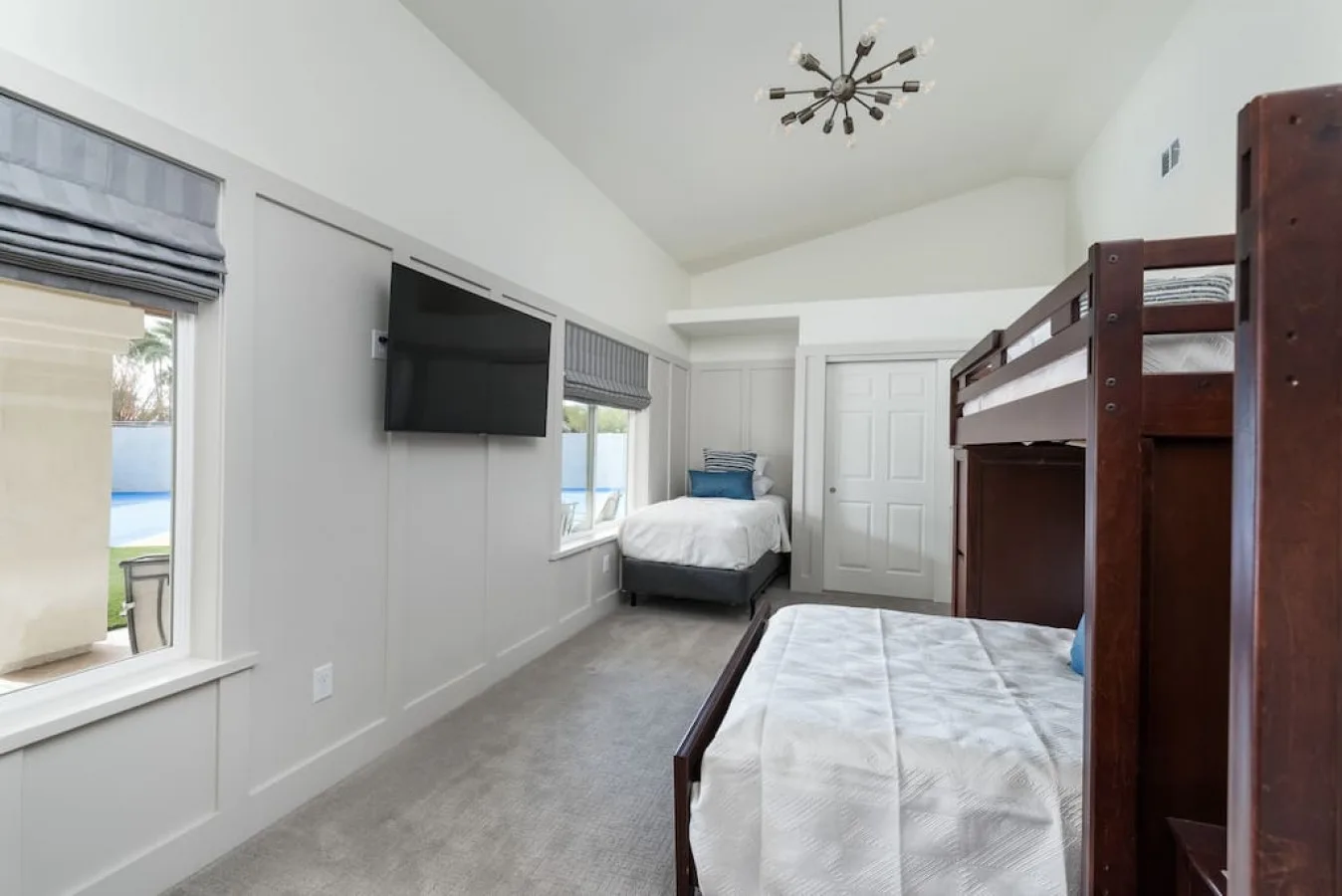 Un dormitorio luminoso con varias camas, un televisor en la pared y ventanas.