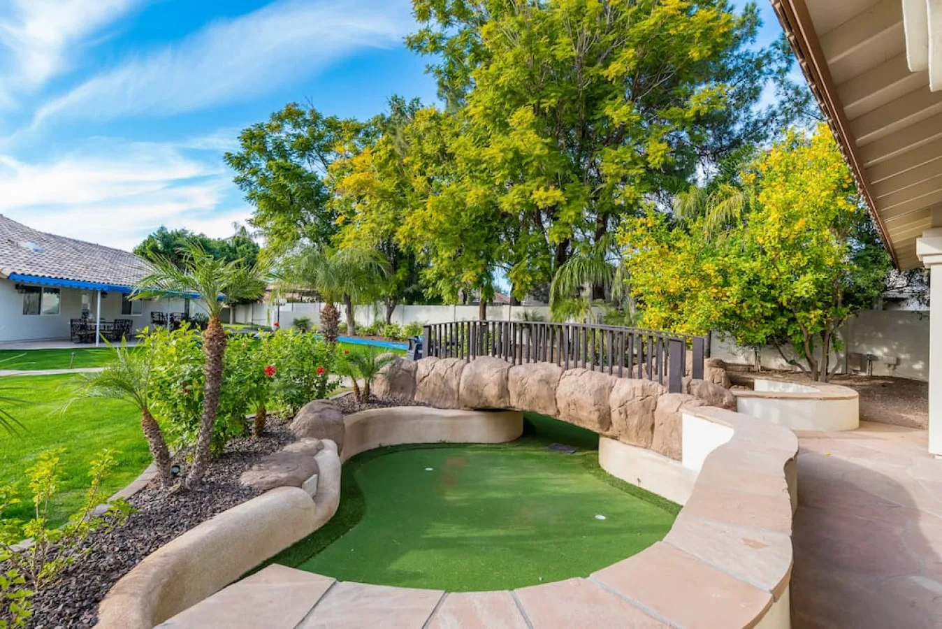 Una piscina en un patio ajardinado está junto a un sendero de piedra y árboles frondosos.