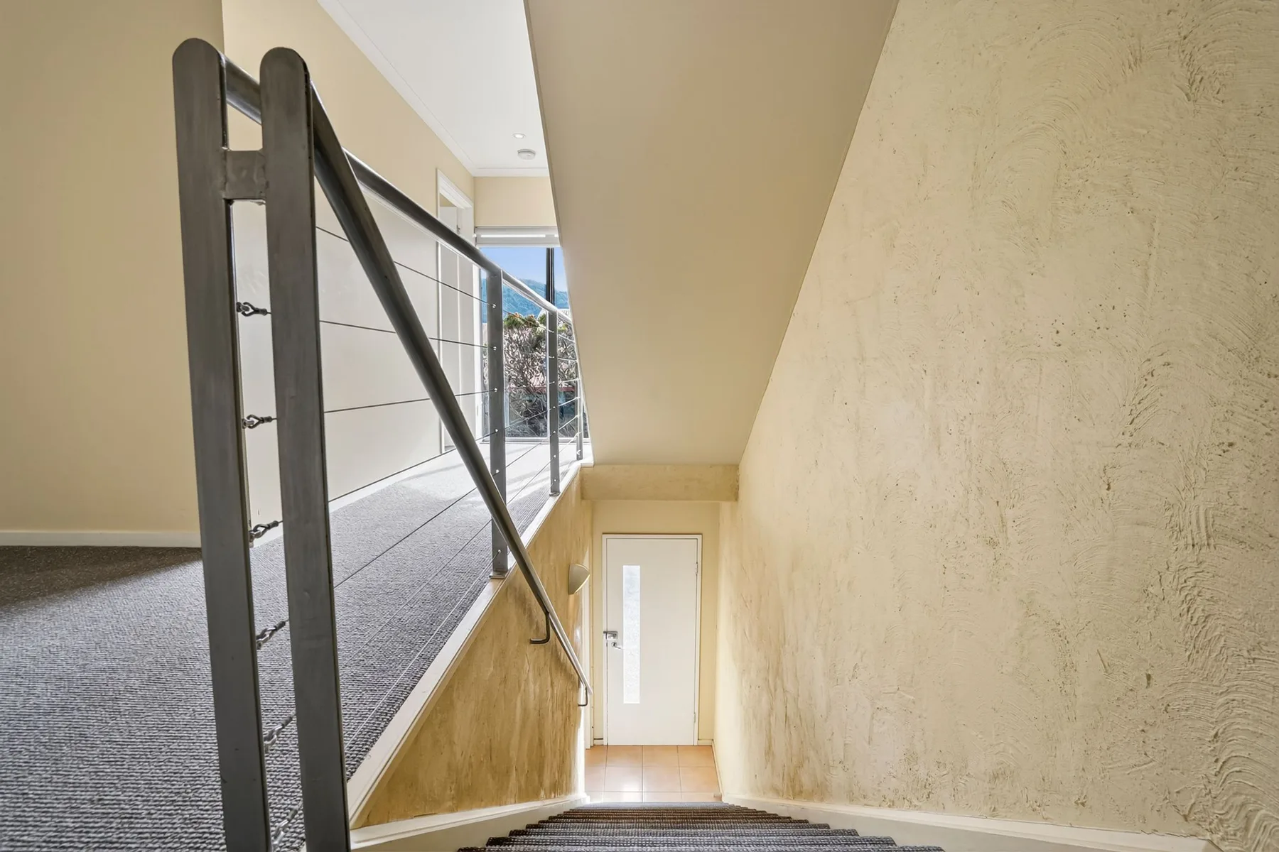 A carpeted staircase descends beside a dark railing and a textured wall.