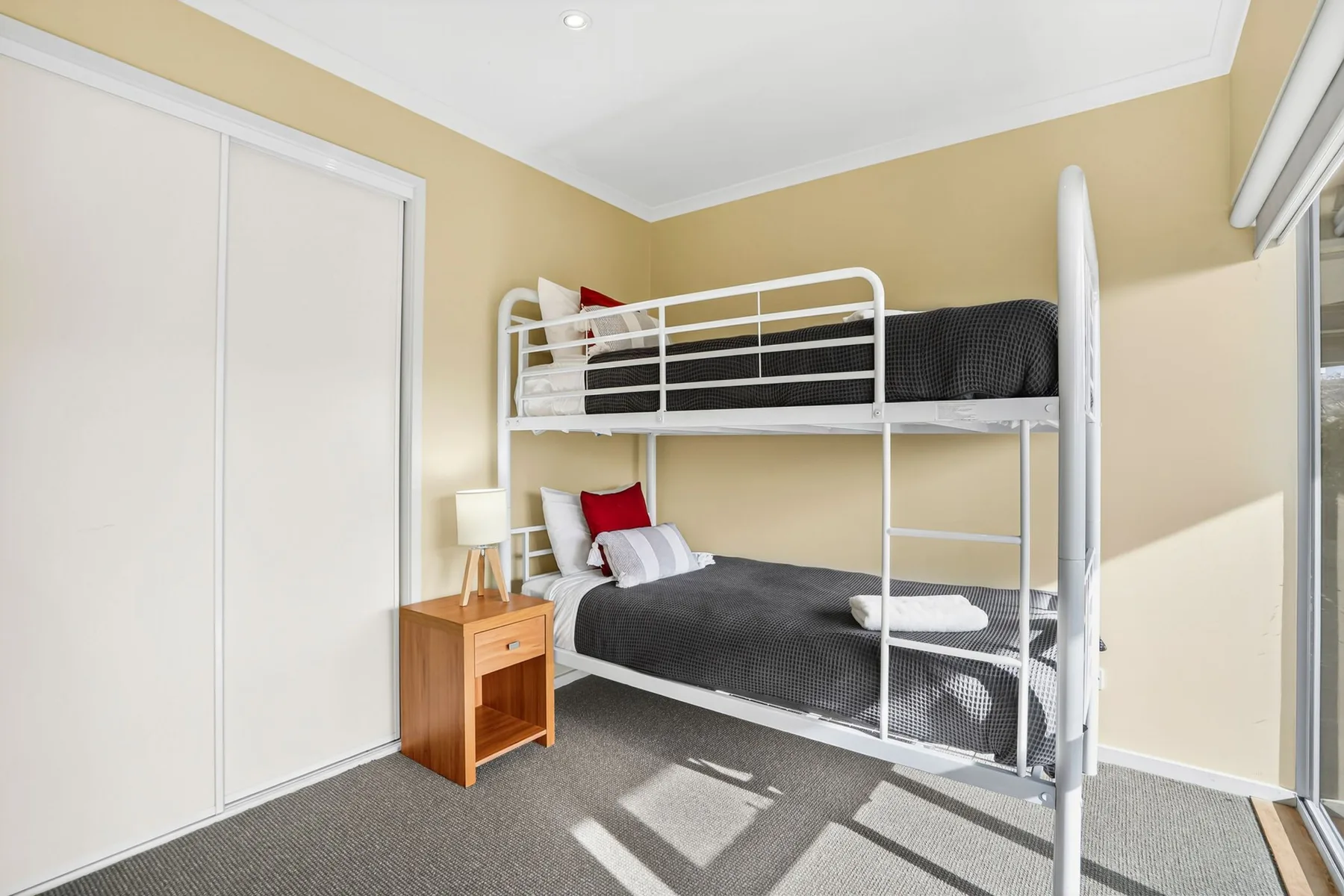A bedroom with a white bunk bed, dark bedding, and a wooden bedside table.