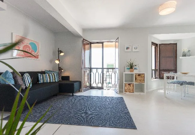 Una sala luminosa con asientos, una alfombra y puertas de vidrio que dan a un balcón.