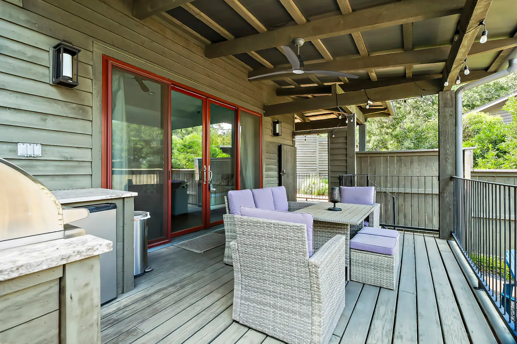 Un patio exterior cubierto con asientos tejidos y una mesa junto a puertas de vidrio.