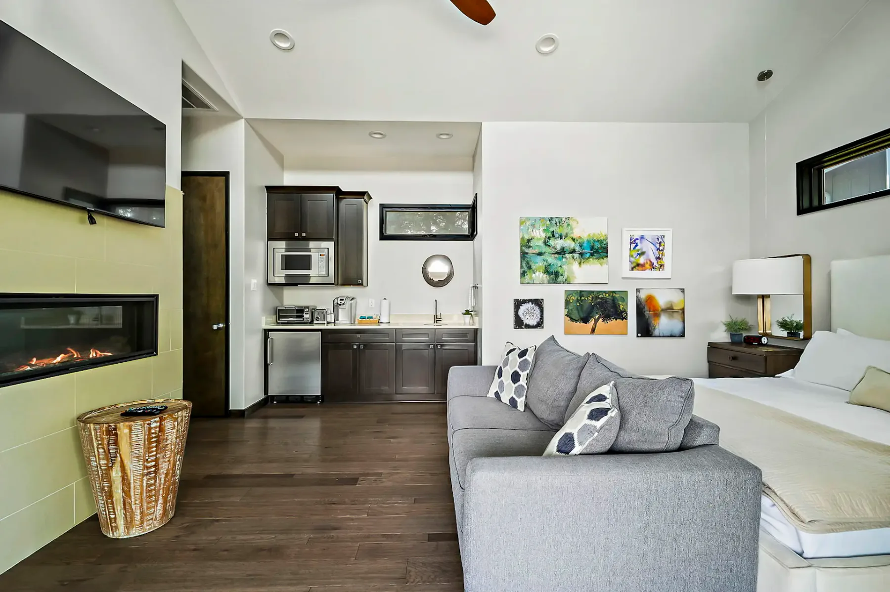 Una sala de estar con asientos grises junto a una cocina compacta y una cama.