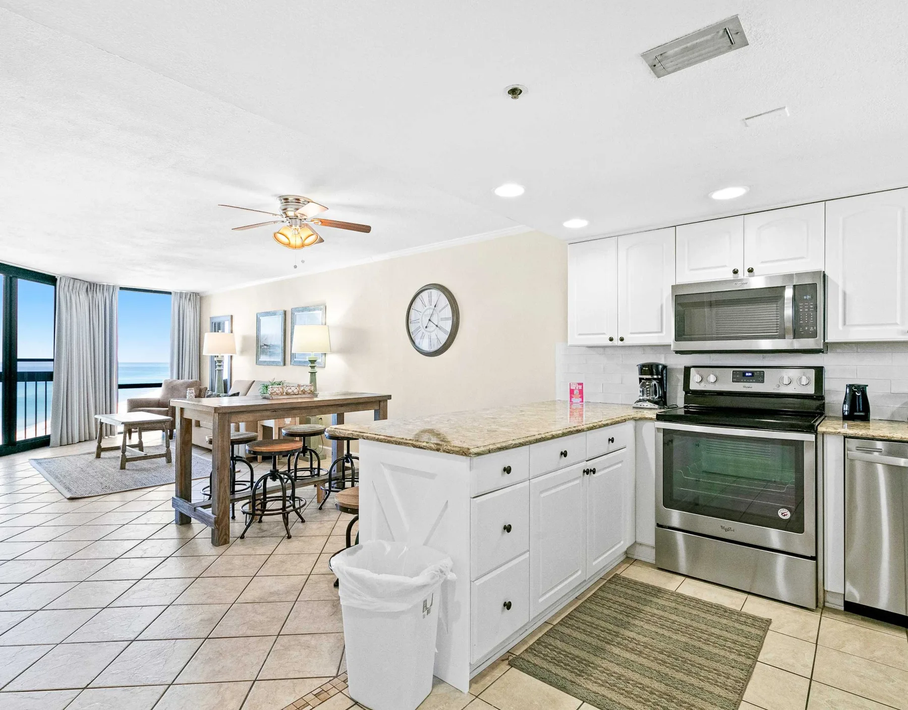 Cocina y comedor abiertos con gabinetes blancos y una mesa junto a grandes ventanas.