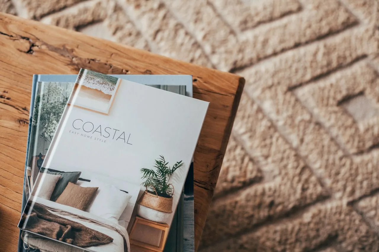 Revistas de diseño costero descansan sobre una mesa de madera junto a una alfombra texturizada.