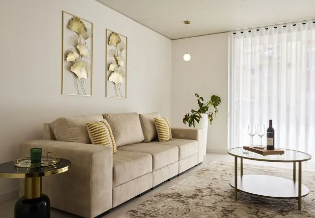 A bright living room with beige seating, a round coffee table, and sheer curtains.
