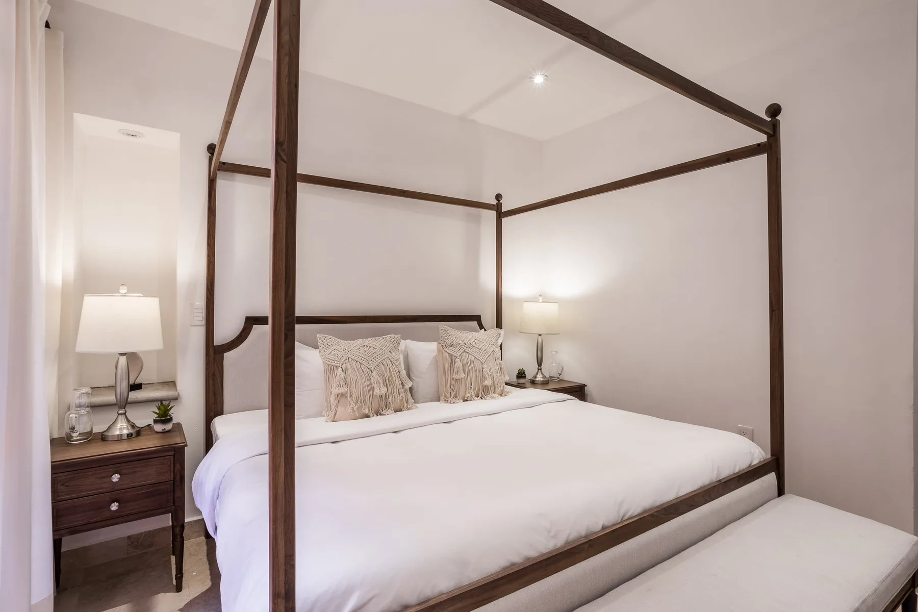 A bedroom with a neatly made four-poster bed and bedside lamps.