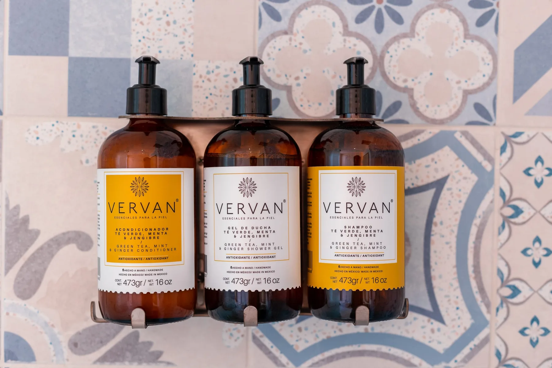 Three amber pump bottles sit against a wall of patterned tiles.