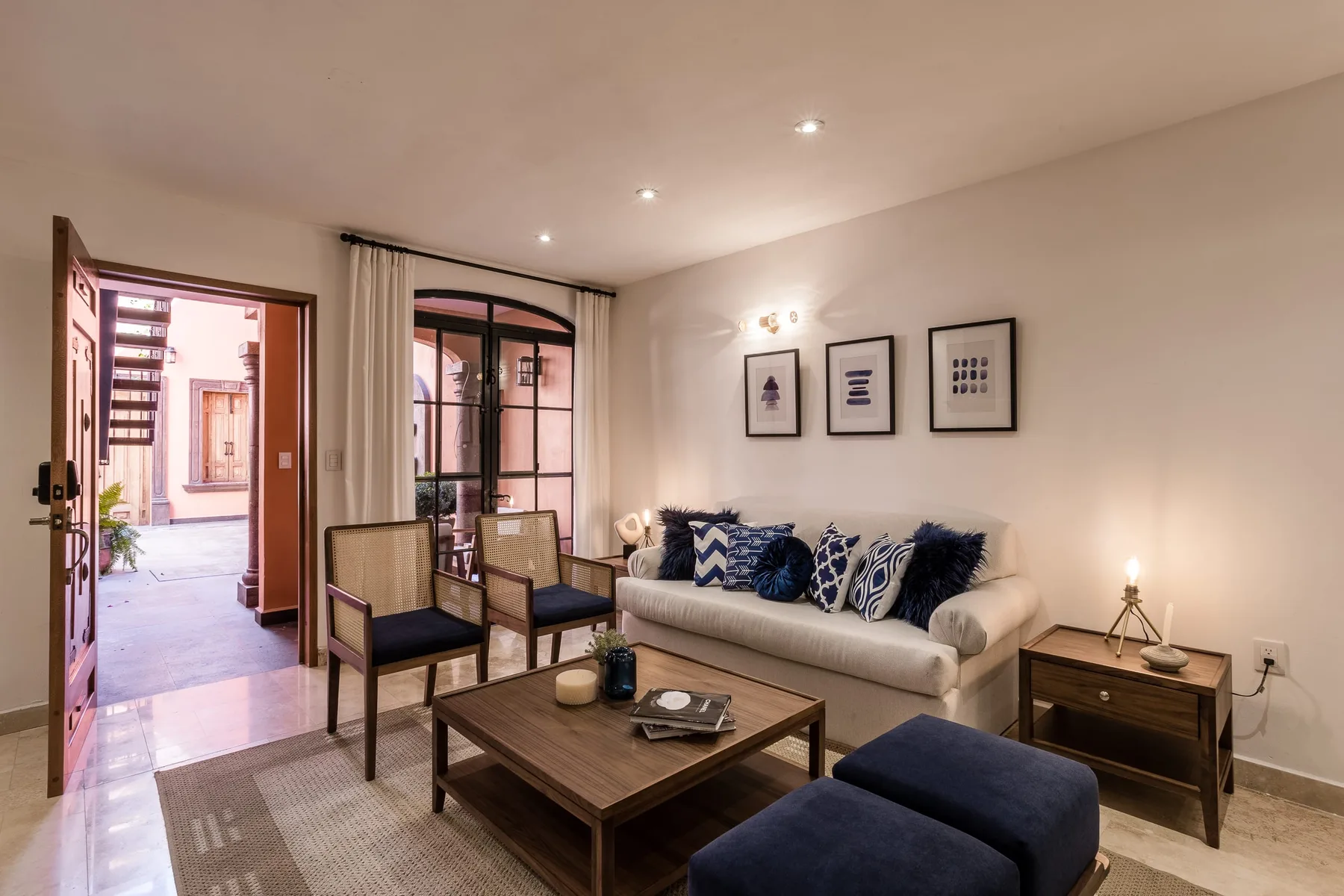 A living room with seating, a coffee table, and an open doorway to a courtyard.
