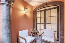 A small seating area with two armchairs and a table sits beside a large arched window.