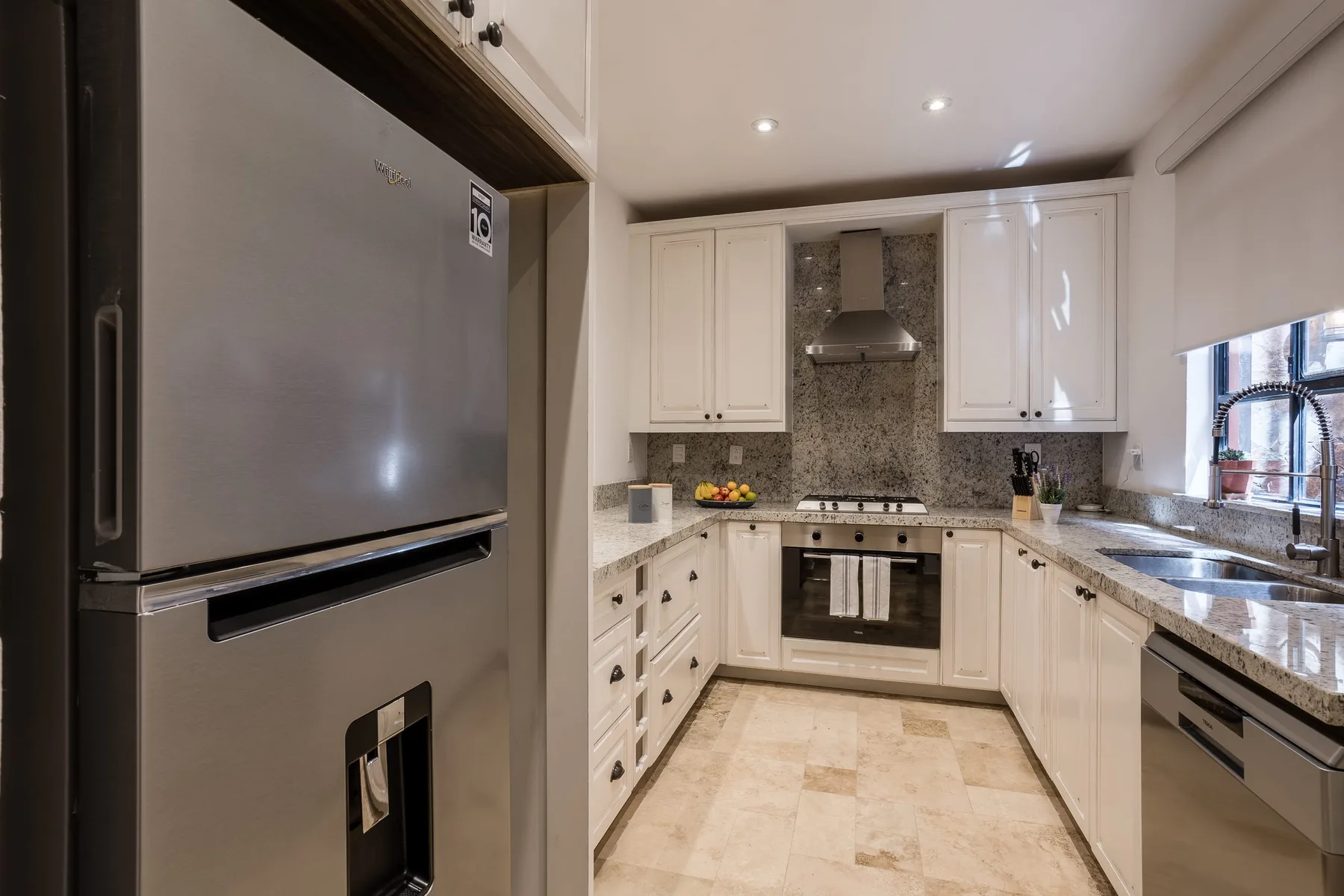 A bright kitchen with white cabinetry, a stove, and a large refrigerator.