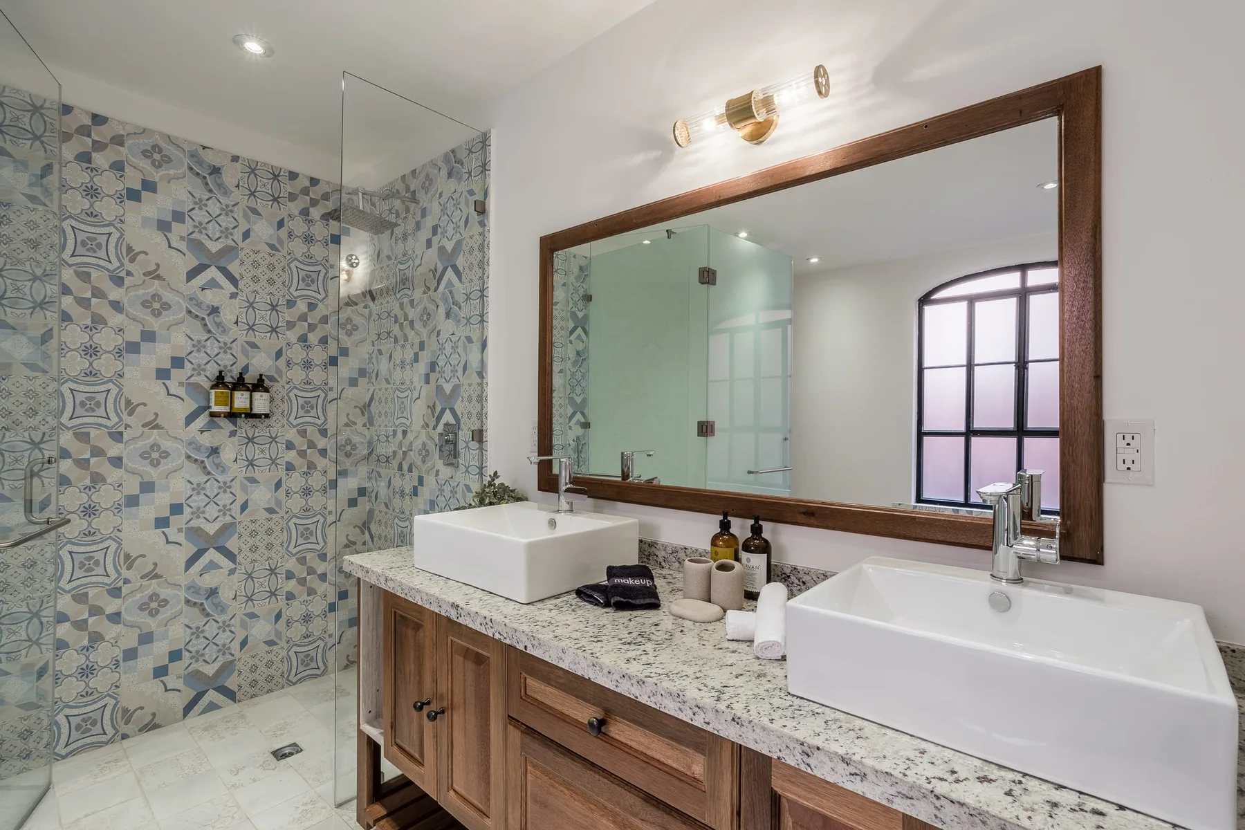 A bathroom vanity with two sinks sits beside a tiled shower.
