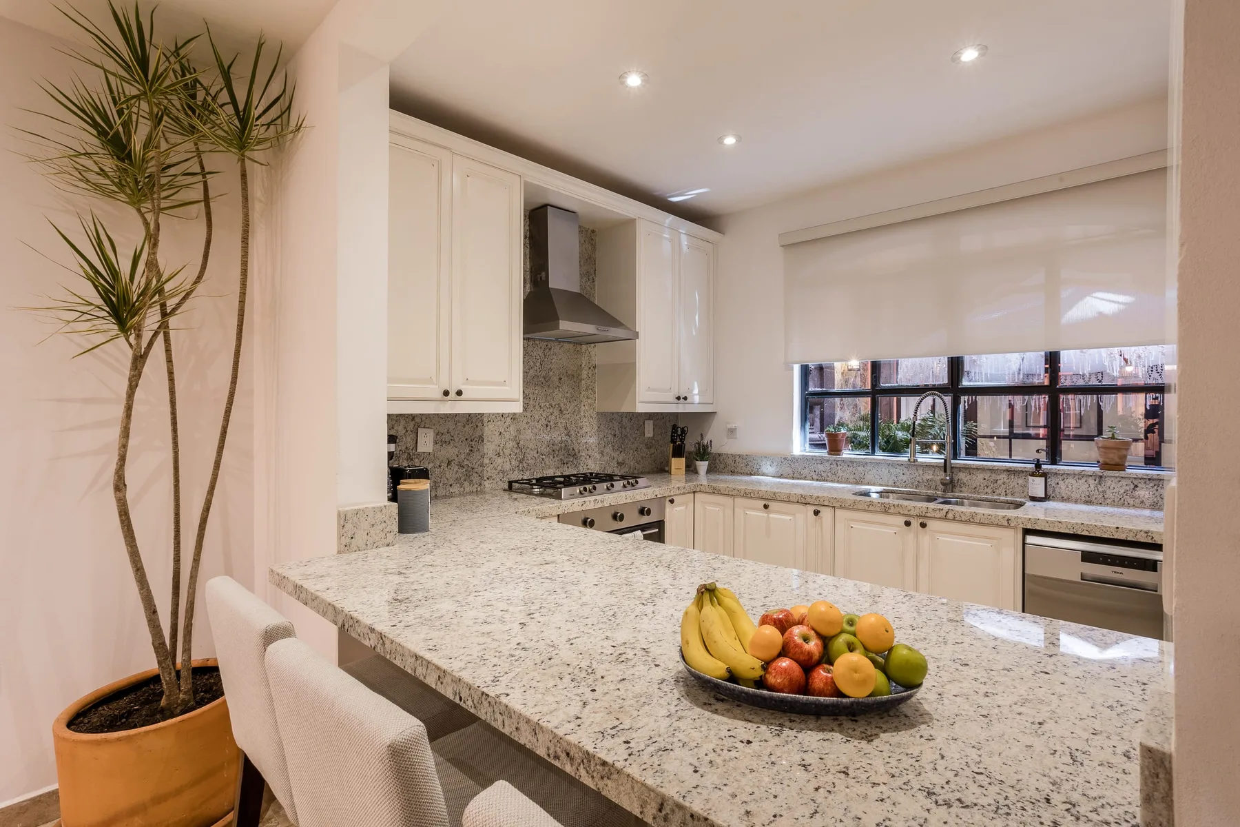 A bright kitchen with a large stone island and a bowl of fruit.