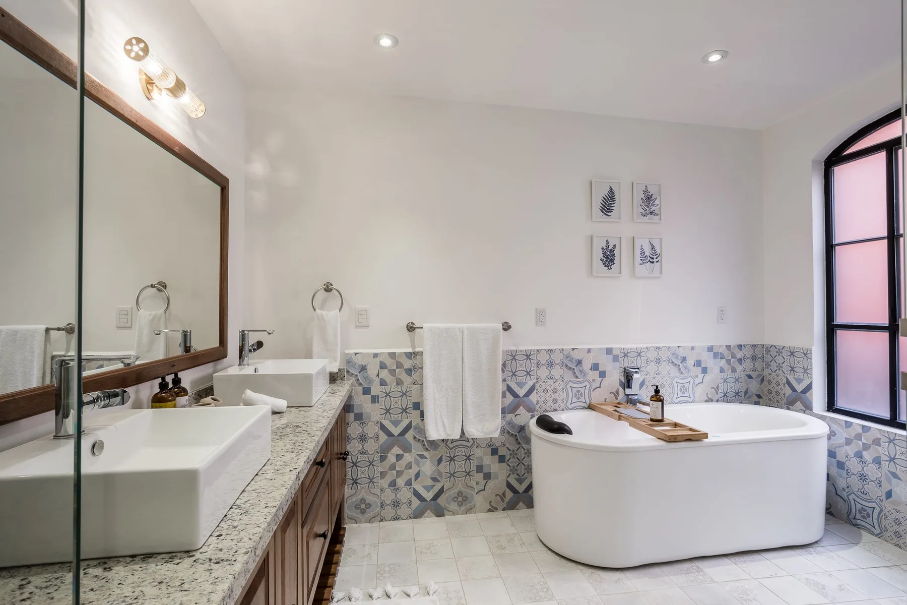 A bright bathroom with a bathtub, two sinks, and patterned wall tiles.