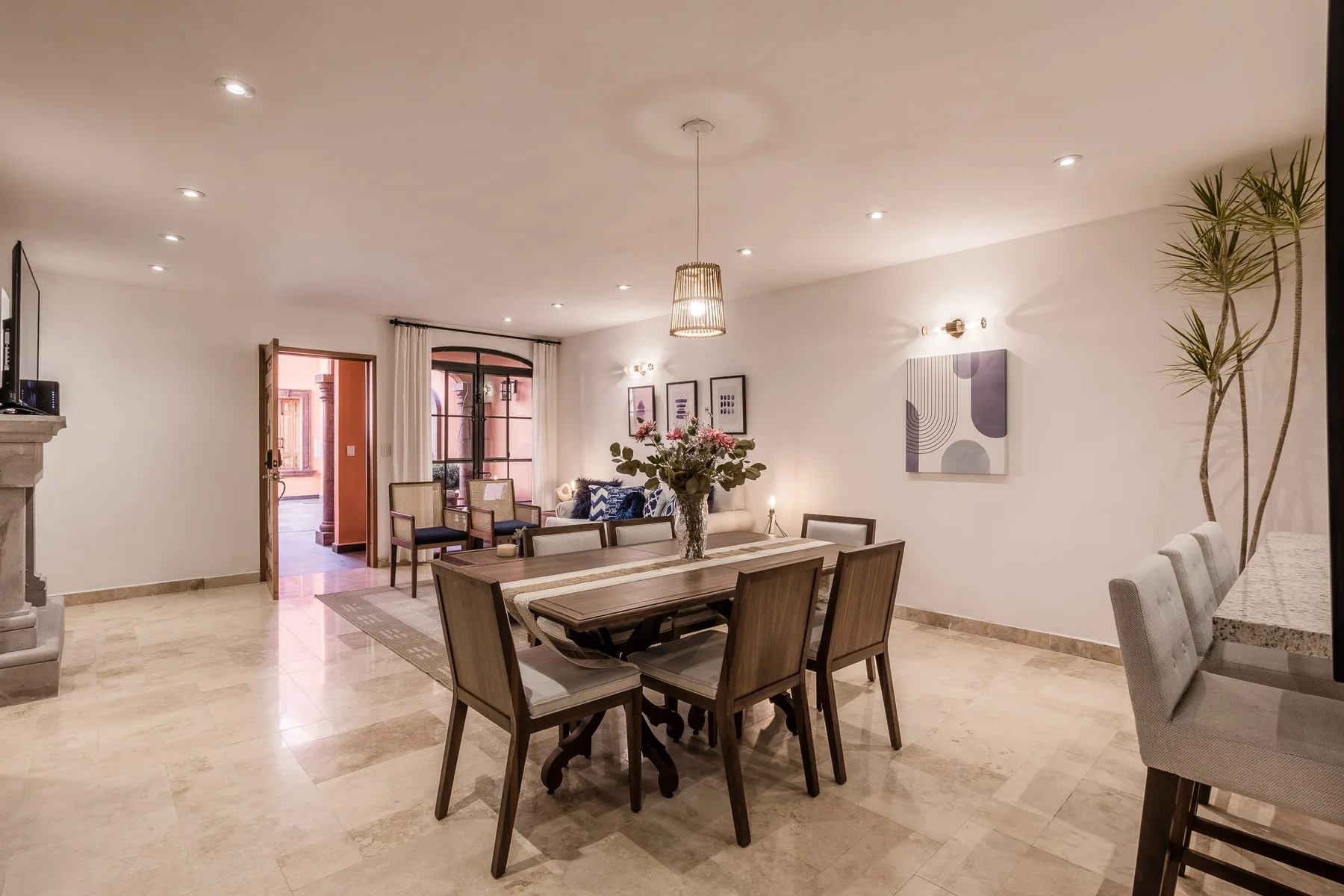 A bright dining area with a wooden table and seating beside a living space.