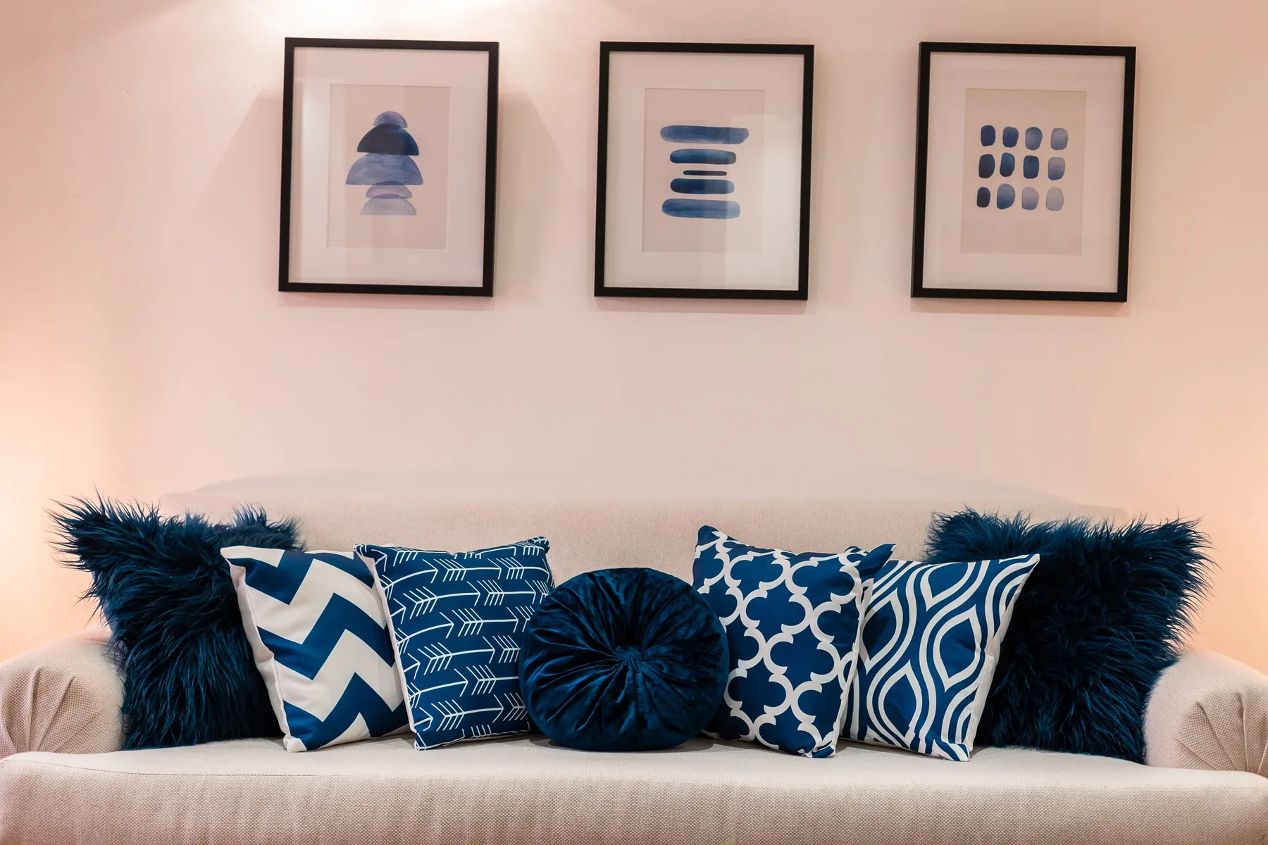 A living room seating area with blue patterned cushions beneath framed artwork.