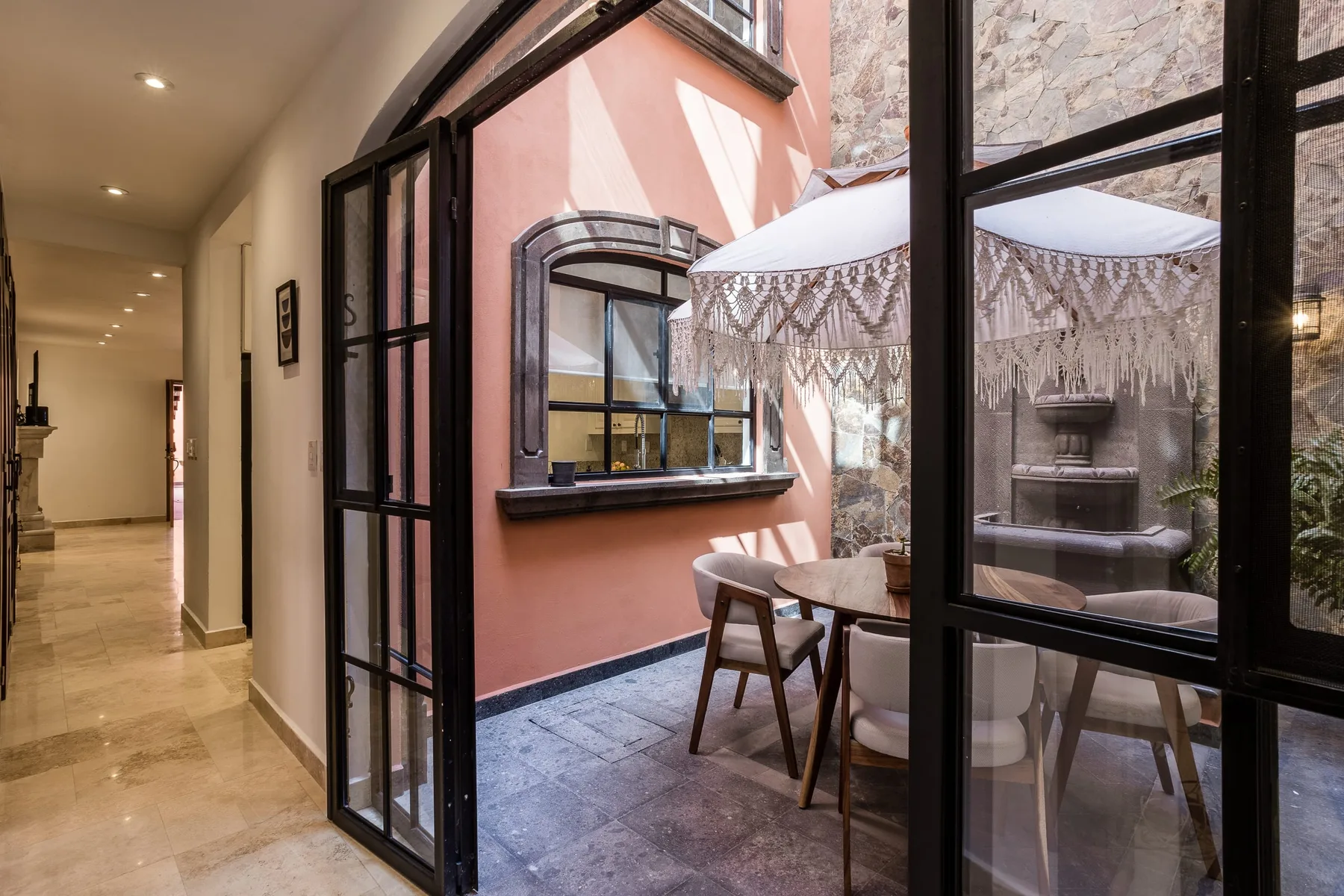 A dining area sits beside a pink-walled courtyard, viewed through glass doors.