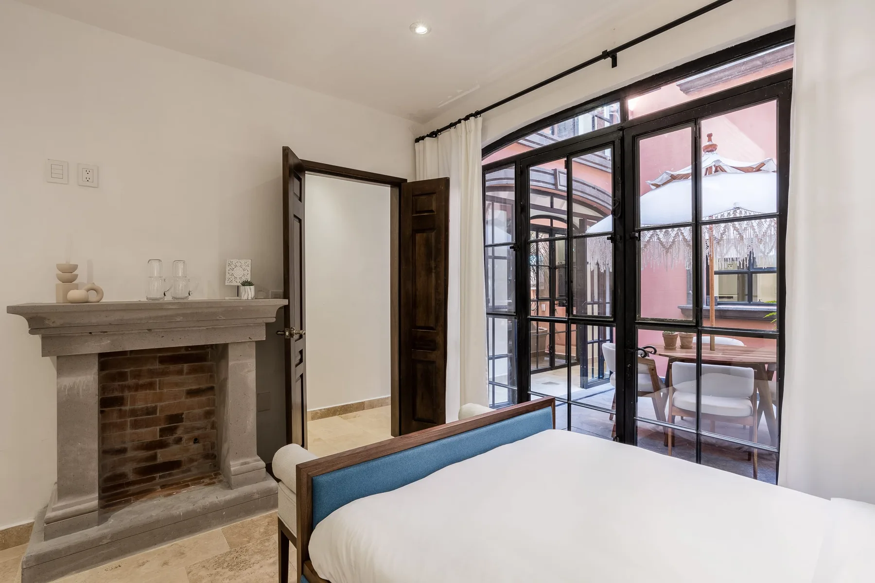 A bedroom with a bed beside a fireplace and glass doors opening onto a patio.