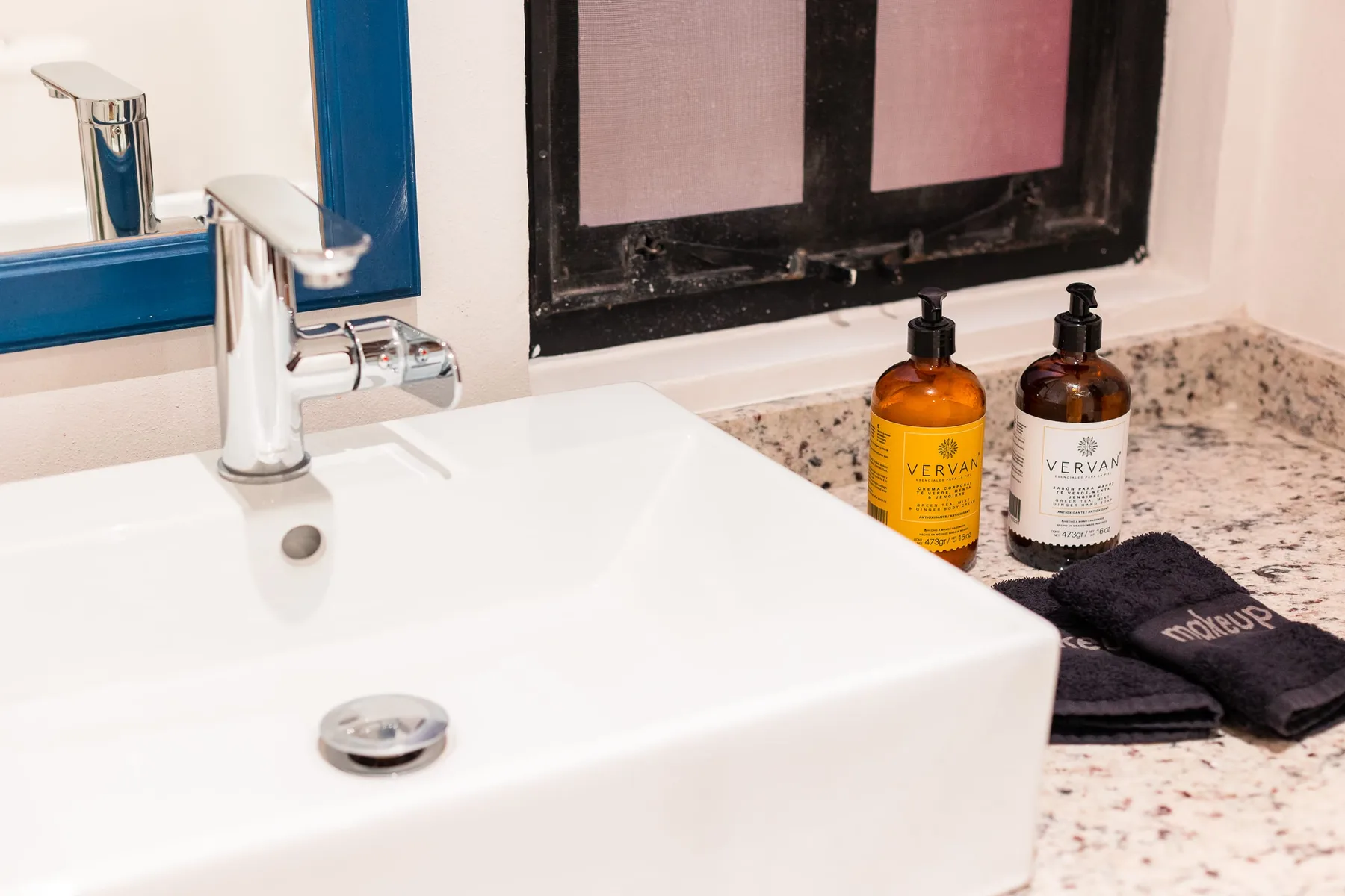 A bathroom sink sits beside soap bottles on a speckled countertop.