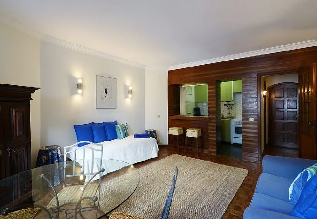 Una sala de estar con un diván blanco, cojines azules y una mesa de centro de vidrio.