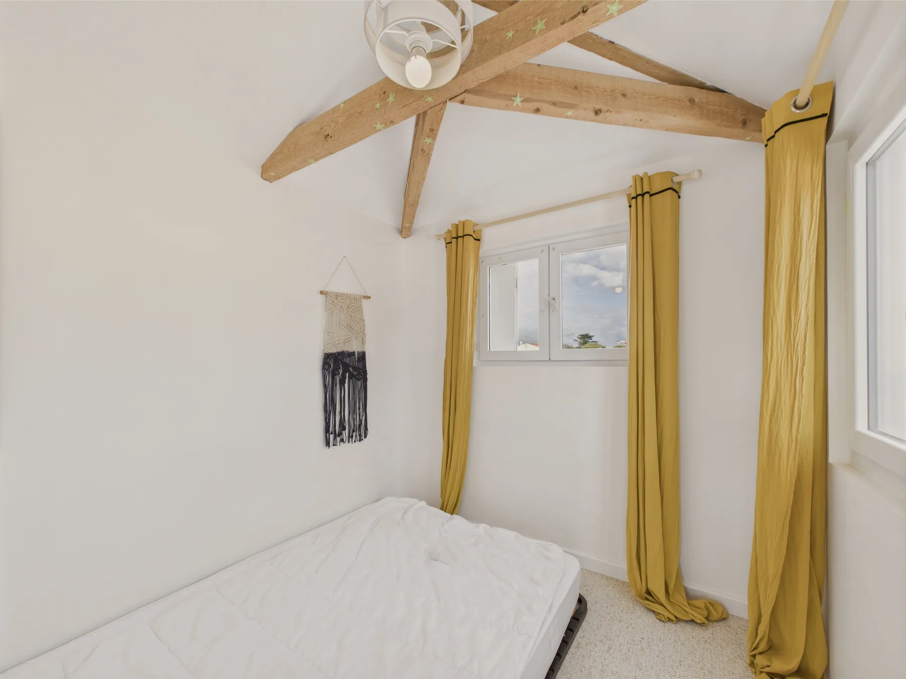 A bright bedroom with a bed beneath exposed wooden ceiling beams.