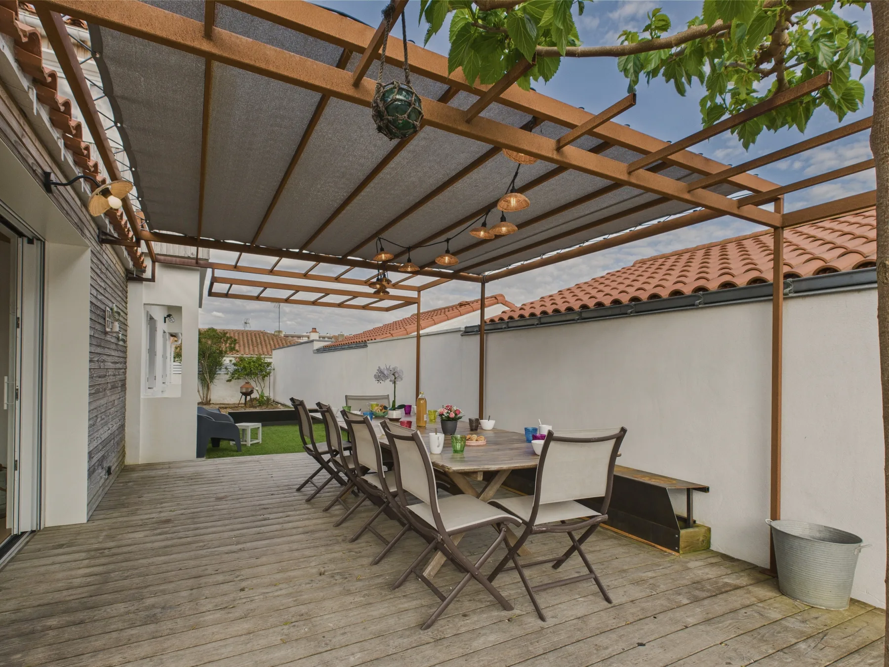 A covered outdoor dining area with a long table and seating beneath a wooden pergola.