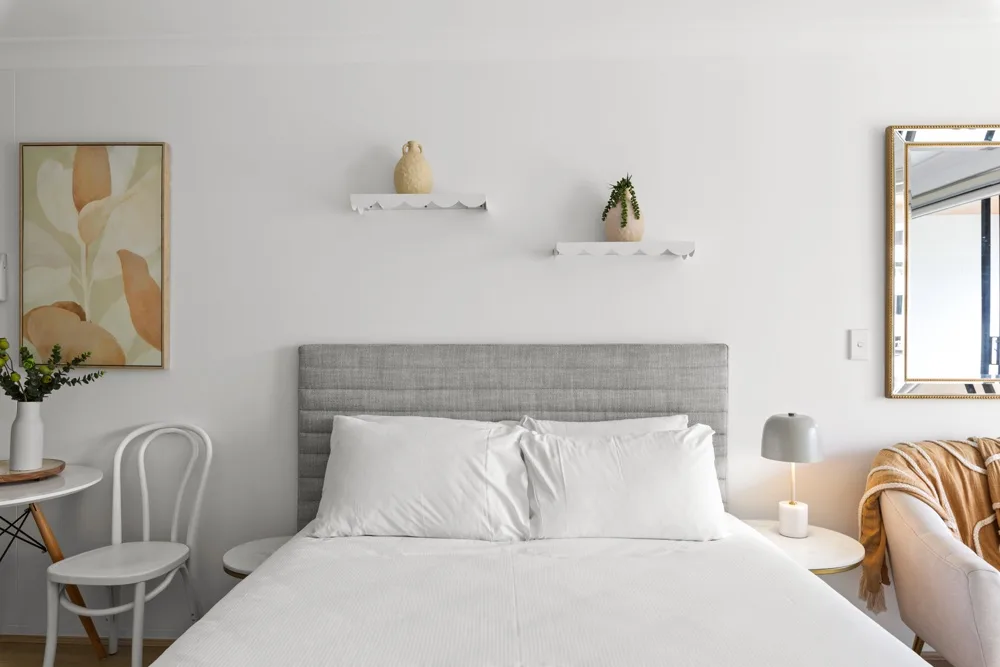 Un dormitorio luminoso con una cama bien tendida y un cuadro en la pared.