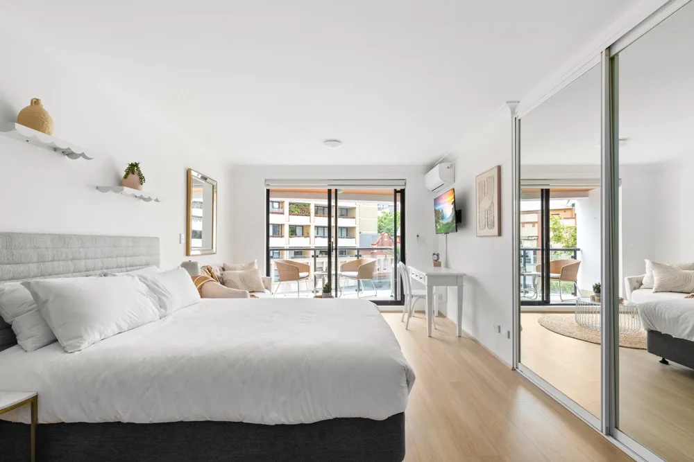 Un dormitorio luminoso con una cama y puertas corredizas de vidrio que dan a un balcón.