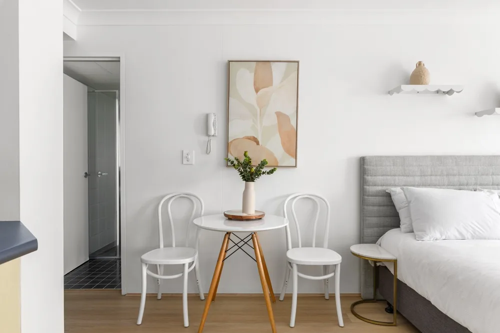 Una luminosa zona de estar en un dormitorio, con una mesa pequeña y dos sillas junto a la cama.