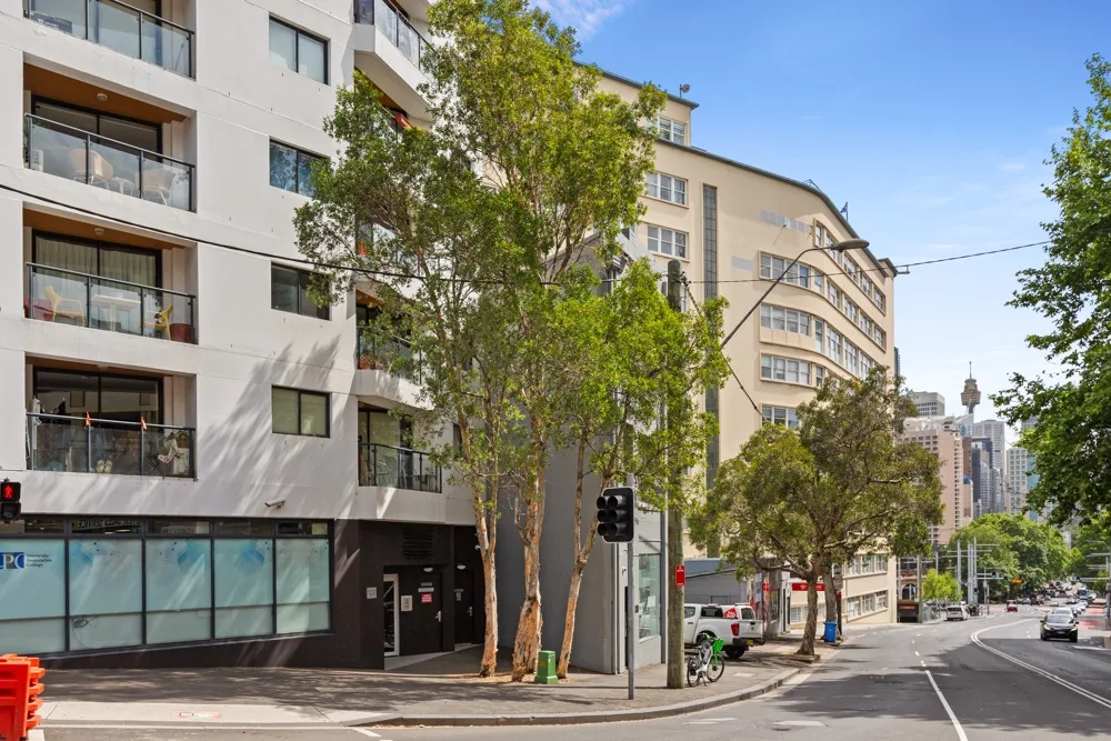 Zona común: Escena de una calle urbana con edificios de apartamentos, árboles y tráfico.