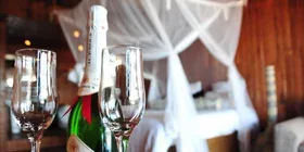 Representative hotel space: A dining table with glassware and a bottle sits in front of a draped bed.