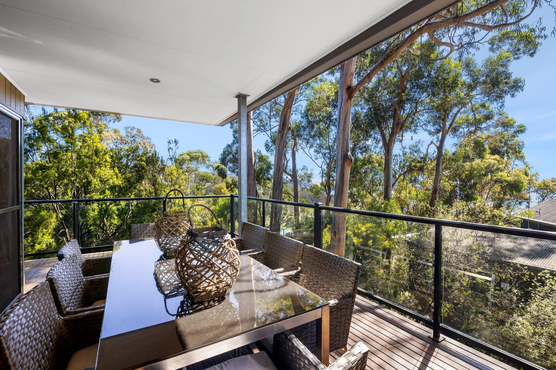 Una zona cubierta de comedor al aire libre con mesa y asientos da a árboles frondosos.