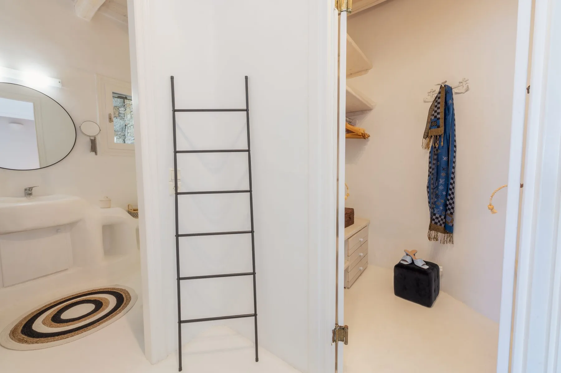 Un baño y una zona de almacenamiento abierta con una escalera apoyada en la pared y ropa colgada.
