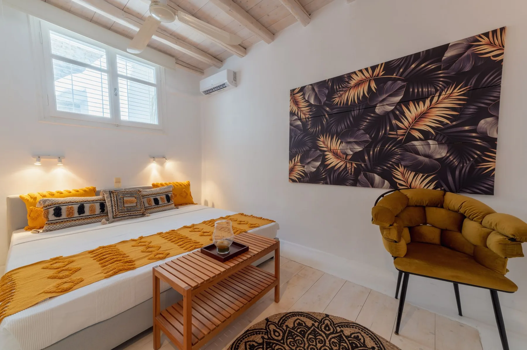 Un dormitorio con una cama, un sillón mostaza y arte botánico en la pared.