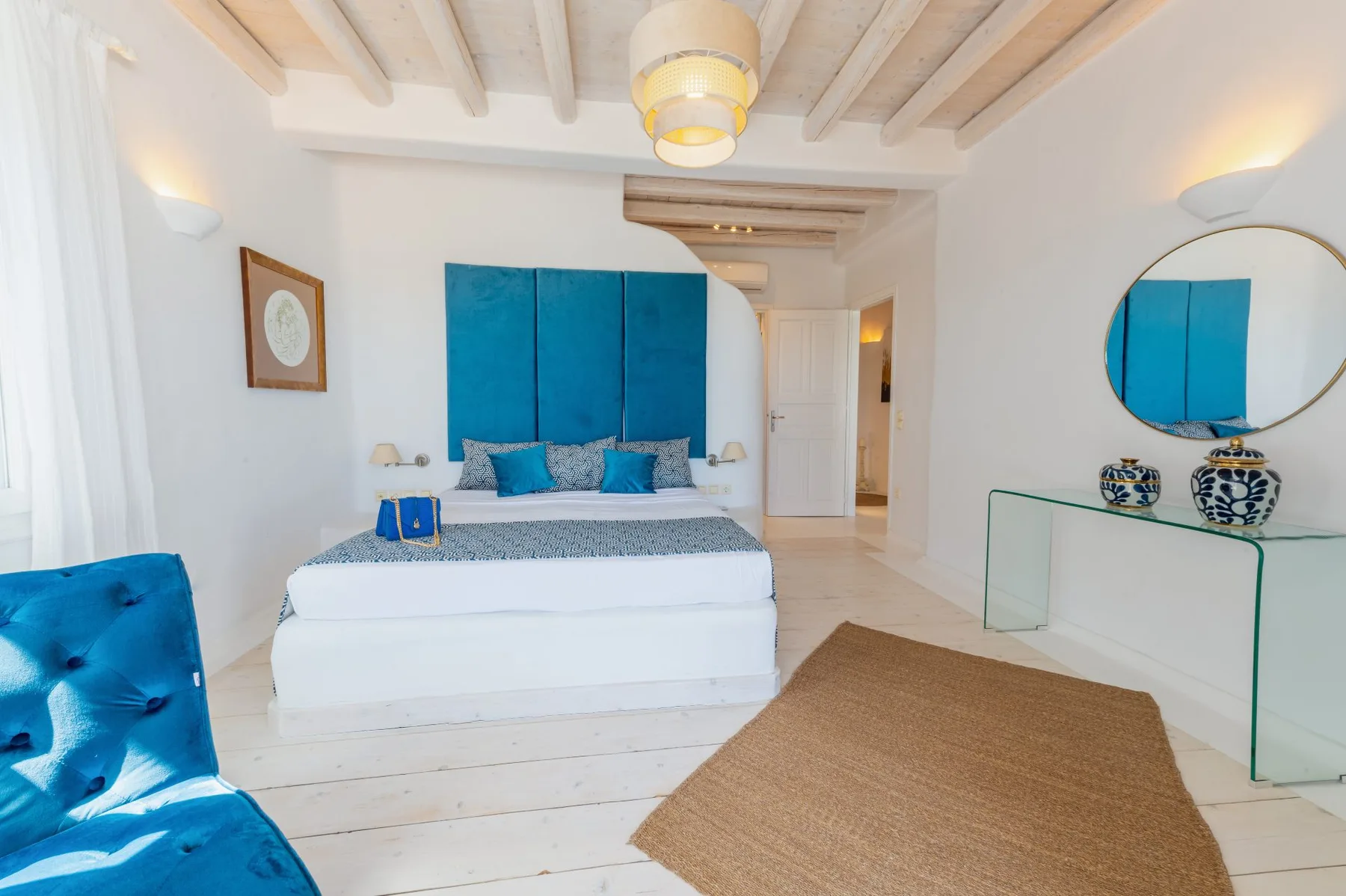 Un dormitorio luminoso cuenta con una cama con ropa de cama azul y una alfombra tejida.