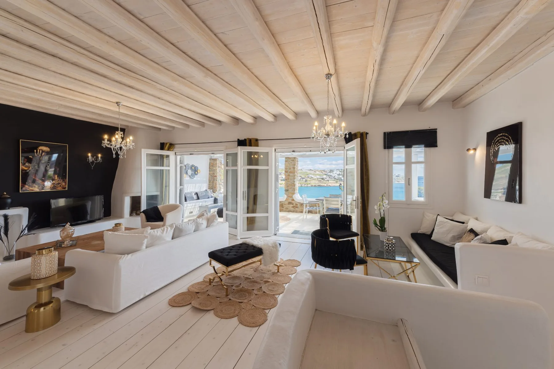 Un salón luminoso con asientos, techo de madera clara y puertas abiertas hacia el mar.