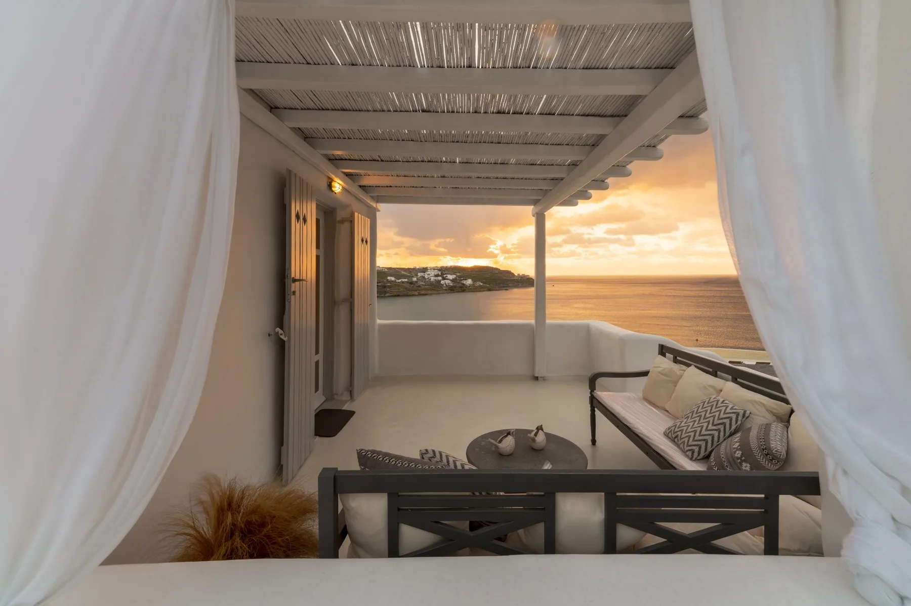 Una terraza cubierta junto al mar se abre al agua, con asientos frente al atardecer.
