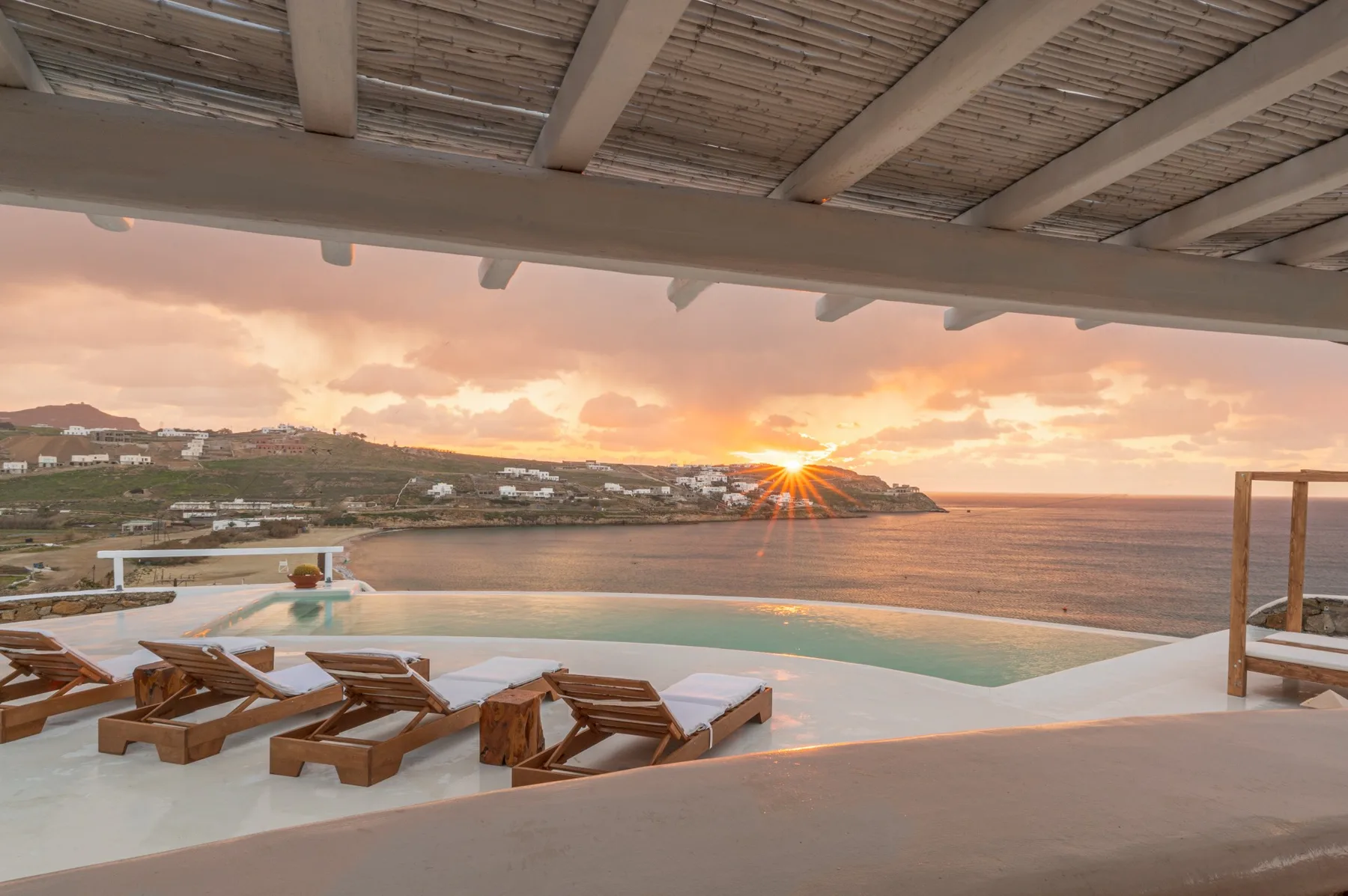 Una terraza con piscina y tumbonas mira al mar al atardecer.
