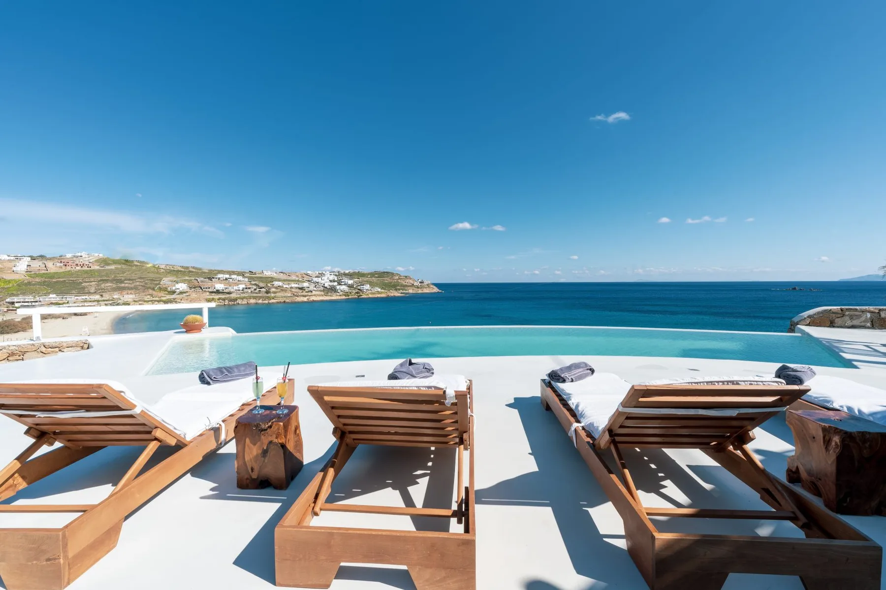 Terraza exterior con asientos de descanso frente a una piscina y el mar.