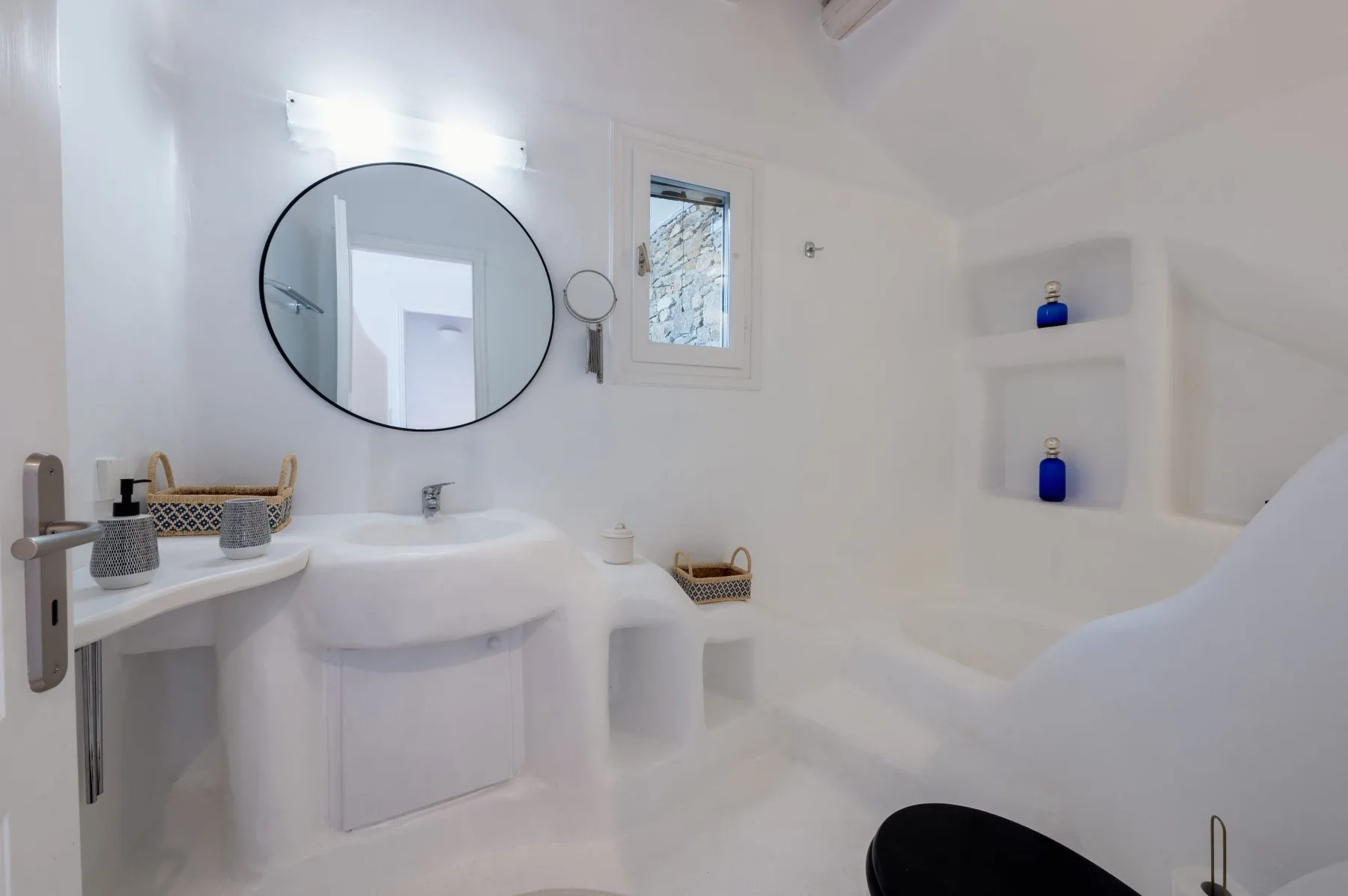 Un baño luminoso con lavabo, espejo redondo y bañera.