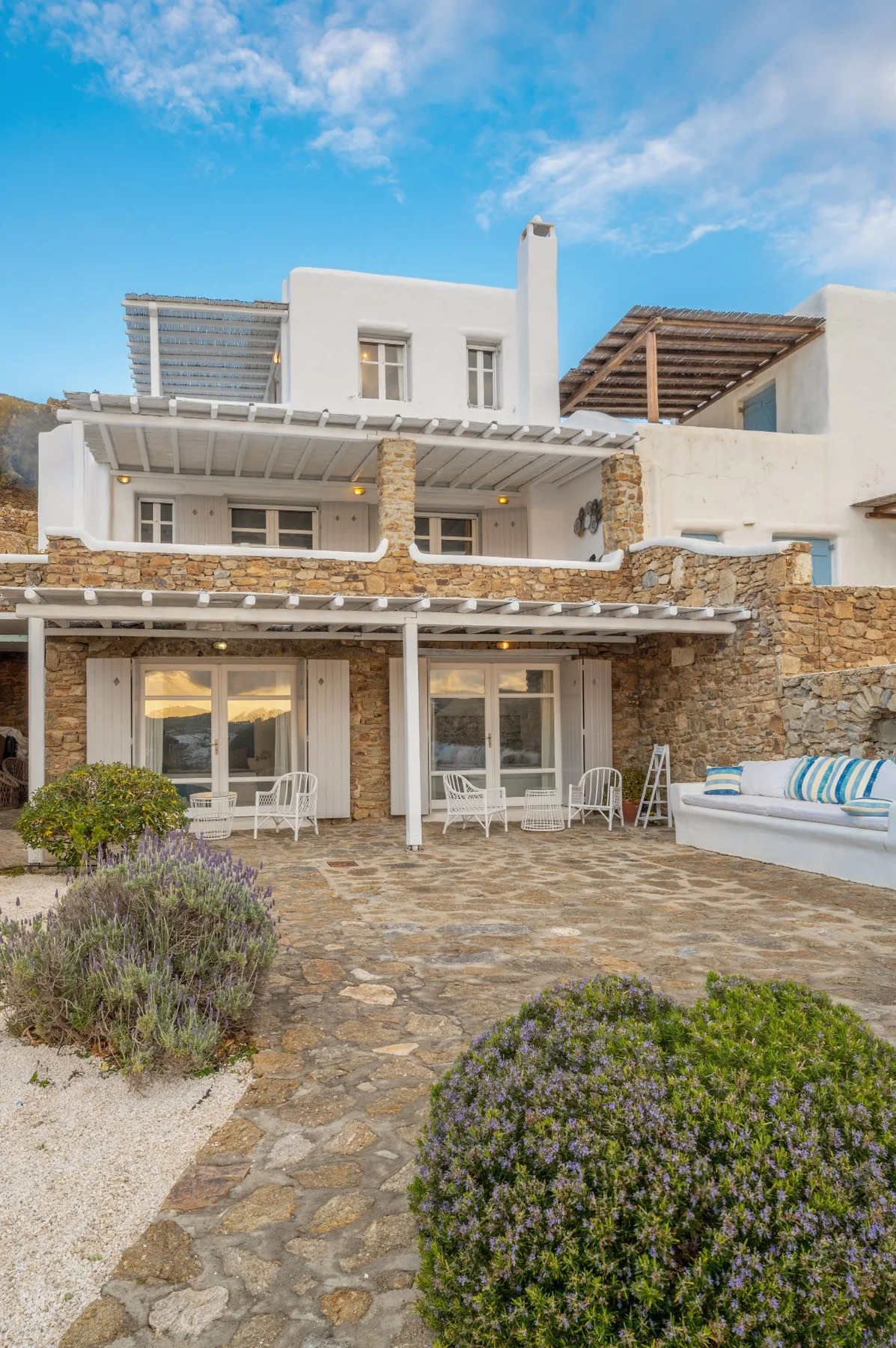 Un edificio blanco con muros de piedra se abre a un patio pavimentado con asientos al aire libre.