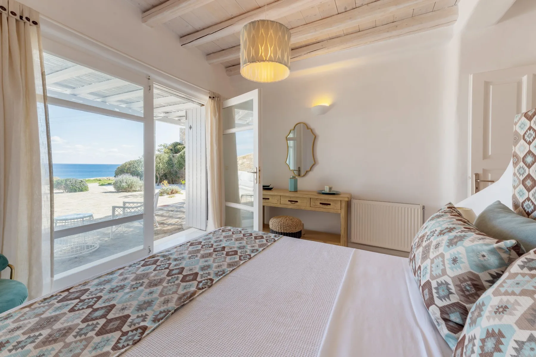 Un dormitorio luminoso con una cama, un escritorio y puertas correderas de cristal con vistas al mar.