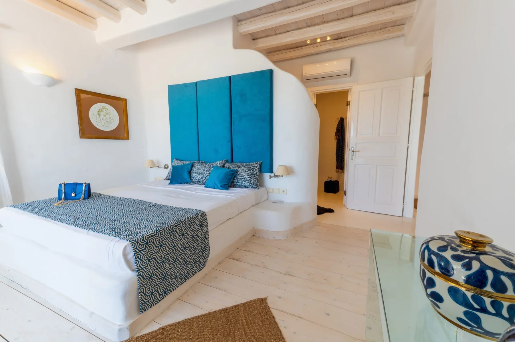 Un dormitorio luminoso con una cama vestida de azul y un armario blanco.
