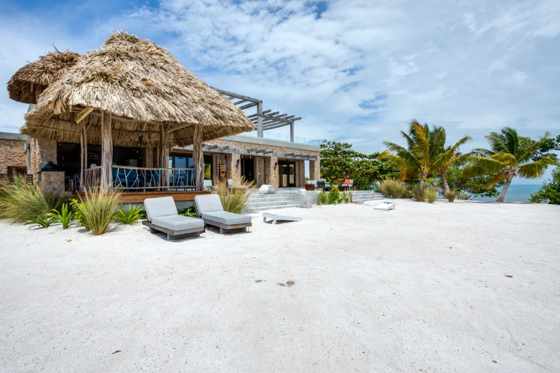 A thatched-roof beachfront building opens onto a sandy outdoor area with lounge seating.