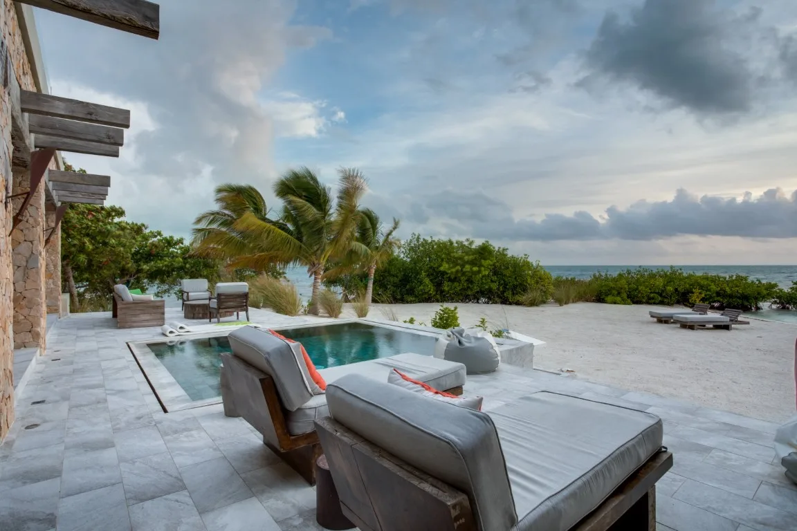 An outdoor poolside lounge with cushioned seating and palm trees by the ocean.